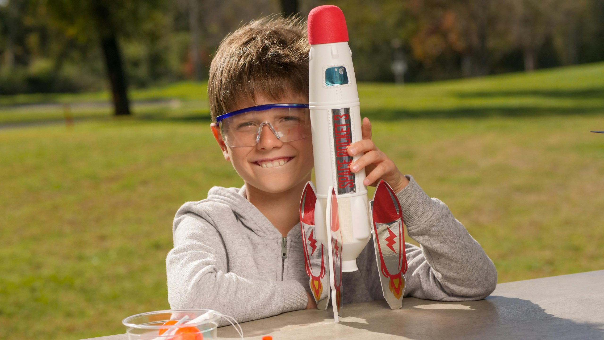 boy in safety goggles proudly holding a toy rocket